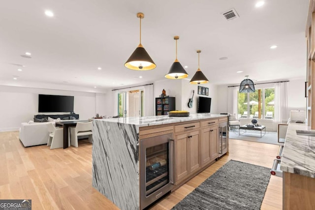 kitchen with hanging light fixtures, light stone countertops, beverage cooler, and a spacious island