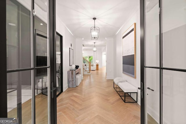 hall with ornamental molding, a chandelier, and light parquet floors