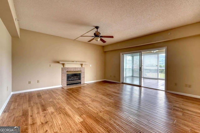 unfurnished living room featuring light hardwood / wood-style floors, ceiling fan, a fireplace, and a textured ceiling