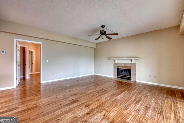 unfurnished living room featuring light hardwood / wood-style flooring, a tiled fireplace, ceiling fan, and a textured ceiling