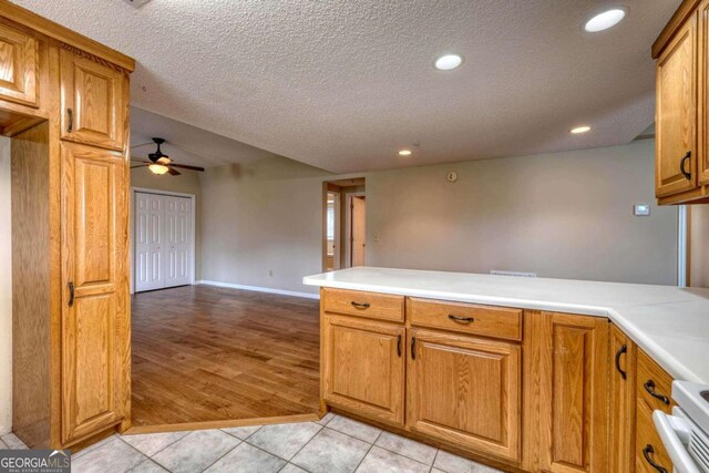 kitchen with range, kitchen peninsula, light wood-type flooring, a textured ceiling, and ceiling fan