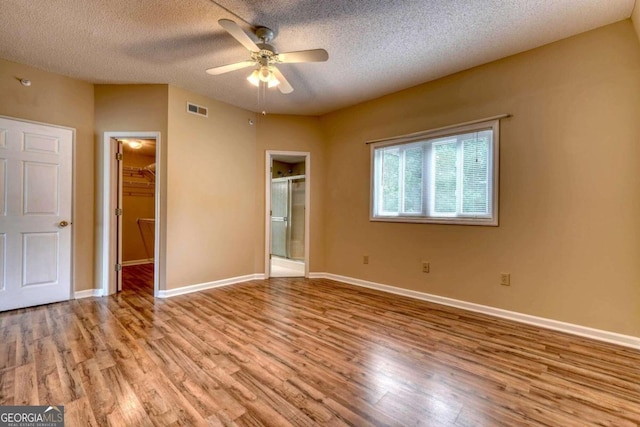 unfurnished bedroom with light wood-type flooring, ensuite bath, ceiling fan, and a walk in closet