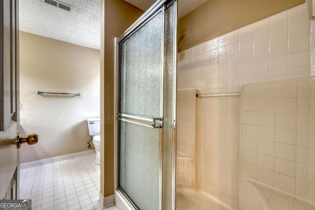 bathroom featuring a textured ceiling, a shower with door, toilet, and tile patterned floors