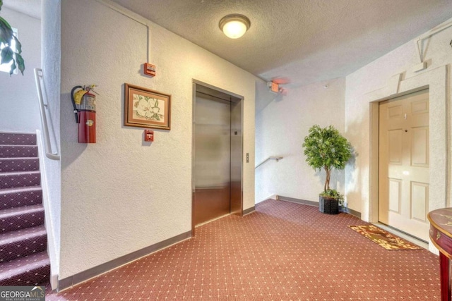 hallway featuring a textured ceiling, elevator, and carpet flooring