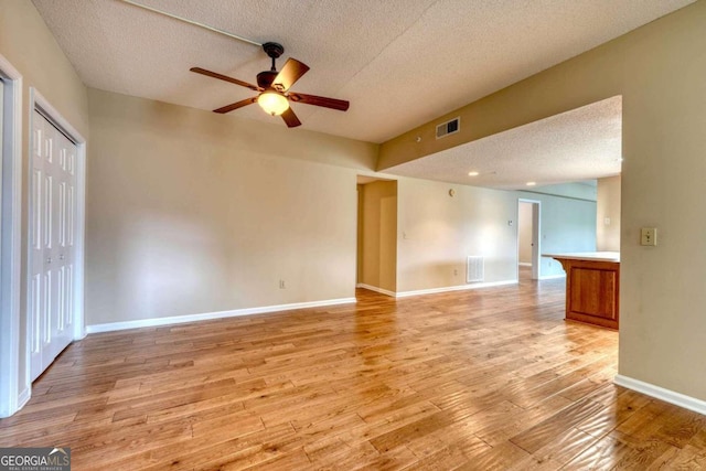 spare room with a textured ceiling, ceiling fan, and light hardwood / wood-style flooring