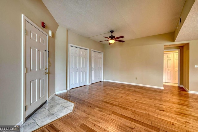 unfurnished bedroom featuring a textured ceiling, light hardwood / wood-style floors, ceiling fan, and multiple closets