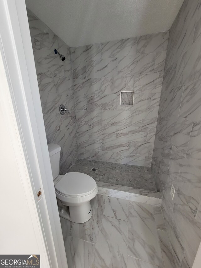 bathroom featuring a tile shower and toilet