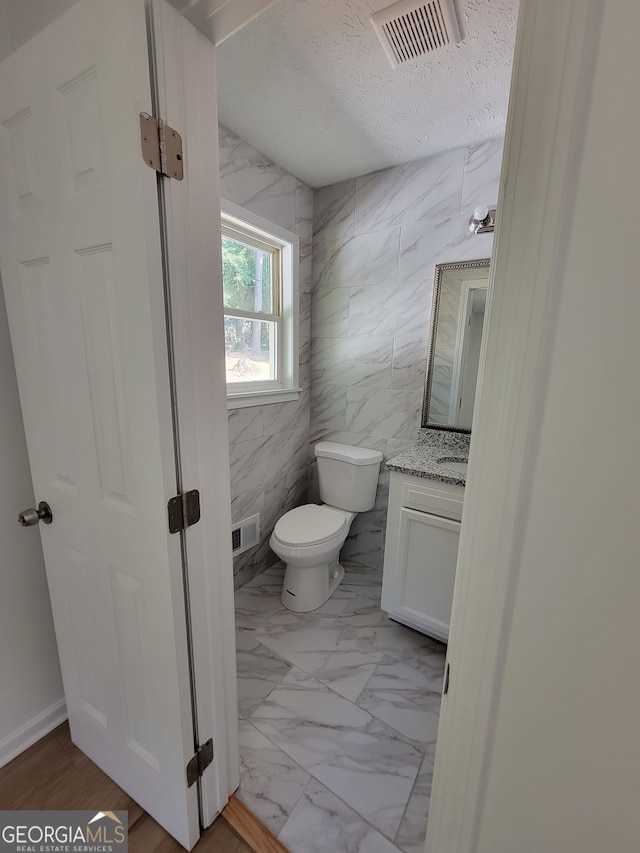 bathroom with vanity, tile walls, toilet, and a textured ceiling