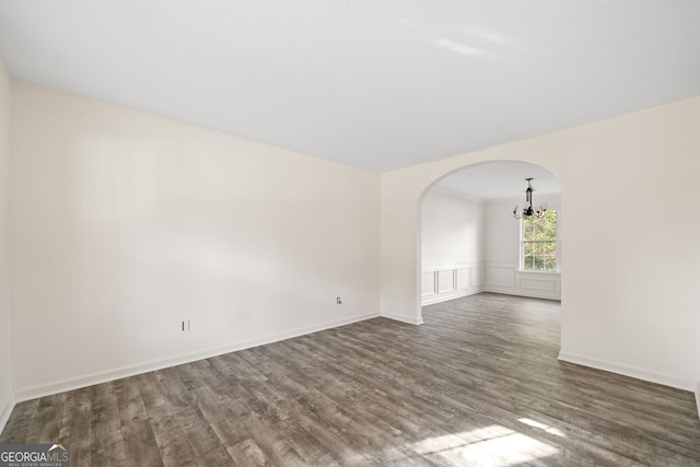 unfurnished room featuring dark wood-type flooring and an inviting chandelier