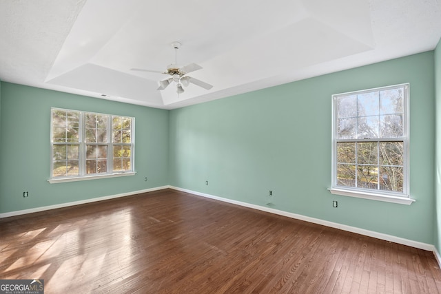 empty room featuring hardwood / wood-style floors, a raised ceiling, ceiling fan, and plenty of natural light