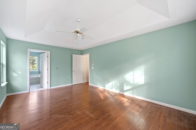 unfurnished bedroom with hardwood / wood-style flooring, ceiling fan, connected bathroom, and a raised ceiling