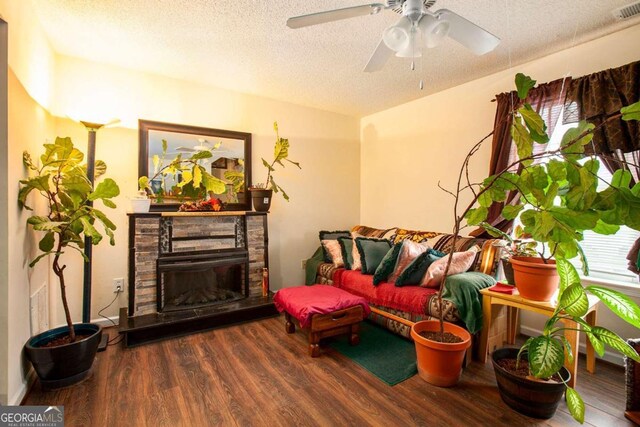 living room with ceiling fan, a textured ceiling, dark hardwood / wood-style floors, and a fireplace