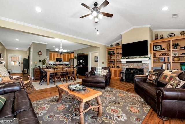 living room with lofted ceiling, ornamental molding, a stone fireplace, light hardwood / wood-style flooring, and ceiling fan with notable chandelier