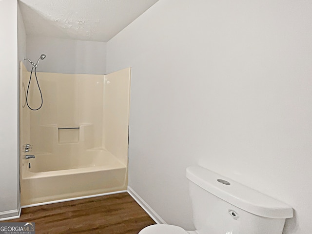 bathroom featuring a textured ceiling, toilet,  shower combination, and hardwood / wood-style flooring