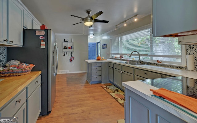 kitchen featuring butcher block counters, light wood-type flooring, crown molding, ceiling fan, and sink