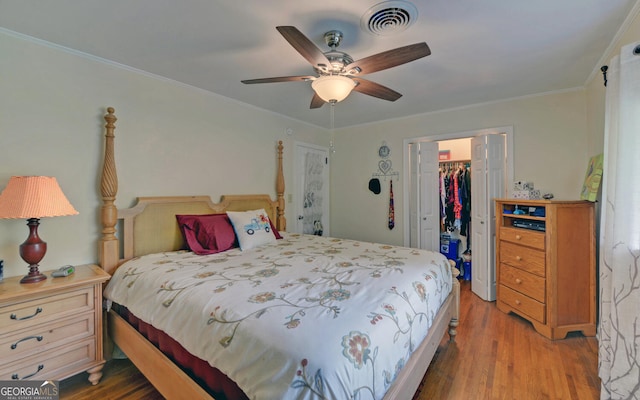 bedroom with a spacious closet, a closet, crown molding, ceiling fan, and hardwood / wood-style flooring