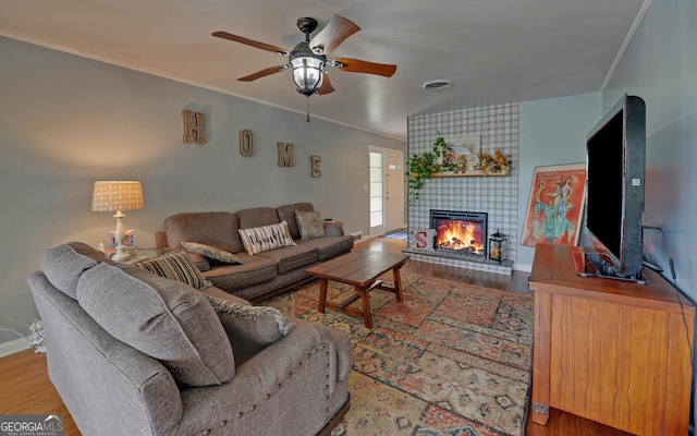 living room with a tile fireplace, ornamental molding, ceiling fan, and hardwood / wood-style flooring