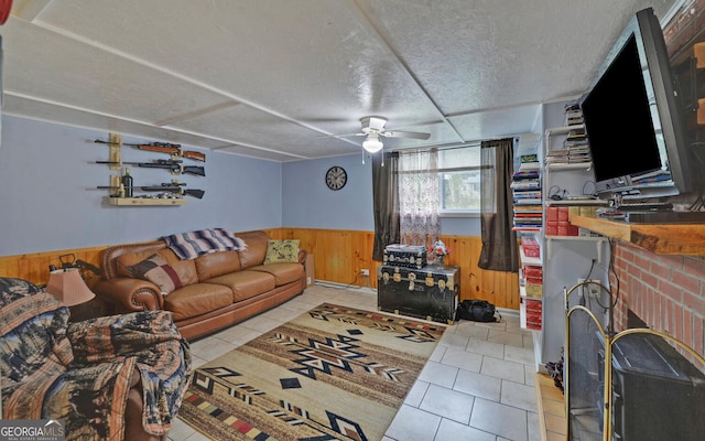 tiled living room featuring a textured ceiling, wooden walls, ceiling fan, and a brick fireplace