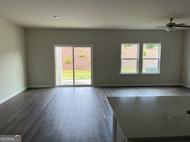 empty room featuring a healthy amount of sunlight, dark hardwood / wood-style flooring, and ceiling fan