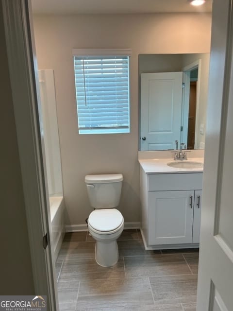 bathroom with wood-type flooring, a tub to relax in, vanity, and toilet