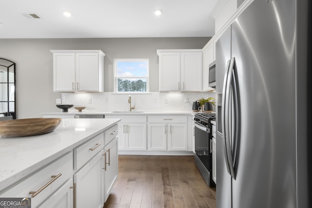 kitchen with sink, tasteful backsplash, white cabinetry, stainless steel appliances, and dark hardwood / wood-style floors