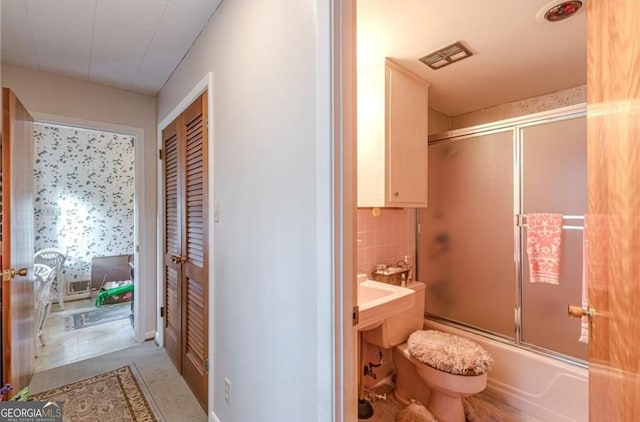 bathroom with tile patterned floors, bath / shower combo with glass door, and toilet