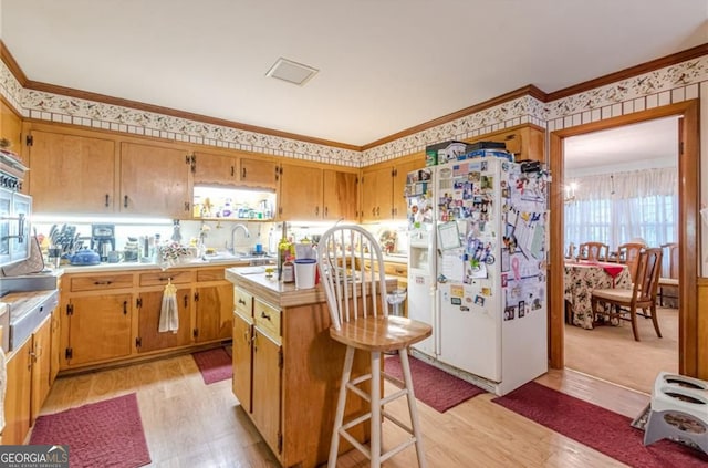 kitchen with white fridge with ice dispenser, a breakfast bar, ornamental molding, light hardwood / wood-style floors, and a center island