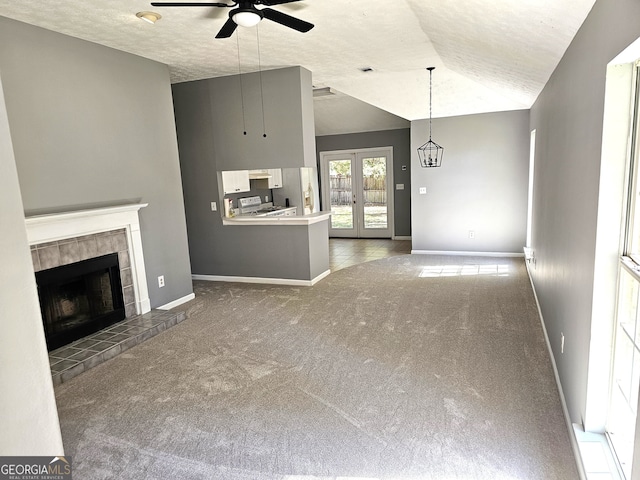 unfurnished living room with a tiled fireplace, vaulted ceiling, dark carpet, and ceiling fan