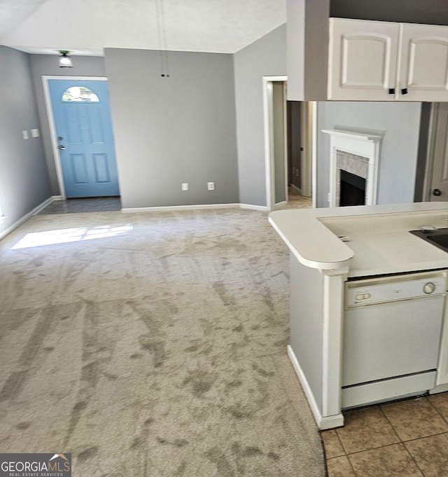 kitchen featuring light carpet, lofted ceiling, white cabinetry, dishwasher, and a tile fireplace