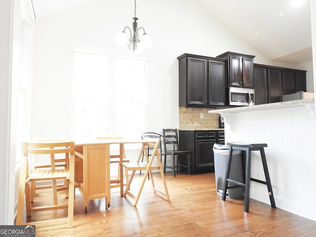 kitchen with decorative backsplash, light hardwood / wood-style floors, light stone countertops, and pendant lighting