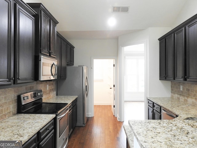 kitchen featuring wood-type flooring, light stone countertops, stainless steel appliances, and decorative backsplash