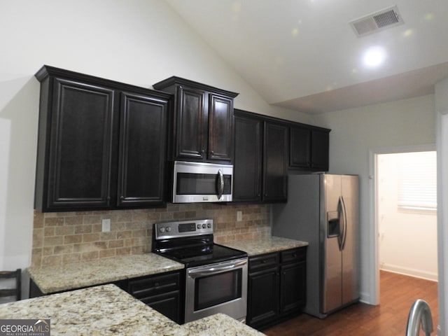 kitchen featuring dark wood-type flooring, appliances with stainless steel finishes, light stone countertops, vaulted ceiling, and decorative backsplash