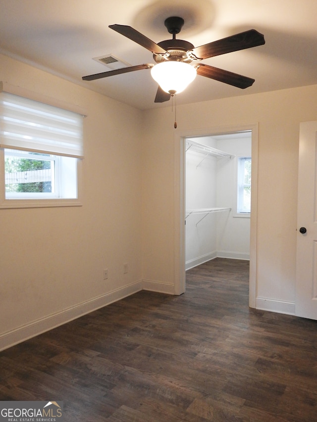 unfurnished bedroom with ceiling fan, a closet, dark wood-type flooring, and multiple windows