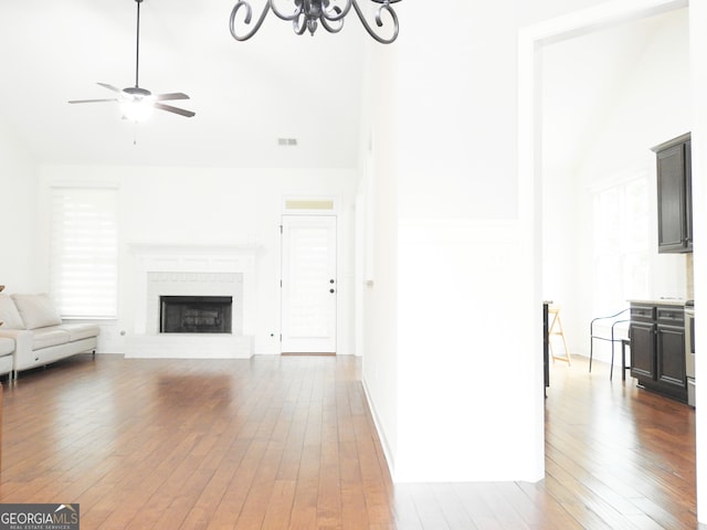 unfurnished living room featuring a brick fireplace, dark hardwood / wood-style flooring, high vaulted ceiling, and ceiling fan