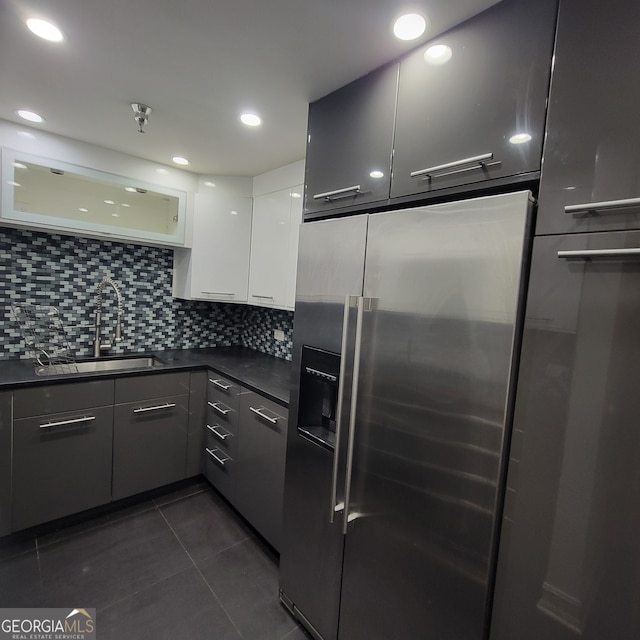 kitchen featuring dark tile patterned floors, backsplash, sink, stainless steel fridge, and white cabinets