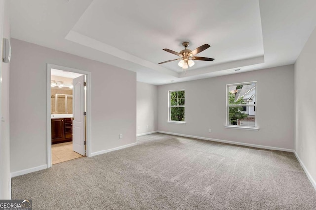 interior space featuring light carpet, connected bathroom, ceiling fan, and a raised ceiling