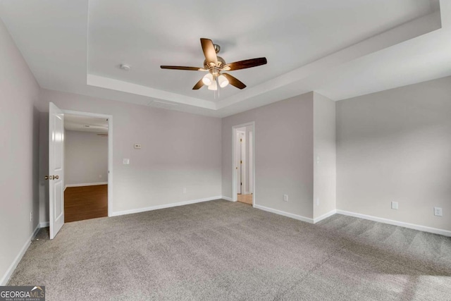 empty room featuring carpet, ceiling fan, and a raised ceiling