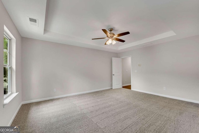 empty room with ceiling fan, a raised ceiling, and carpet