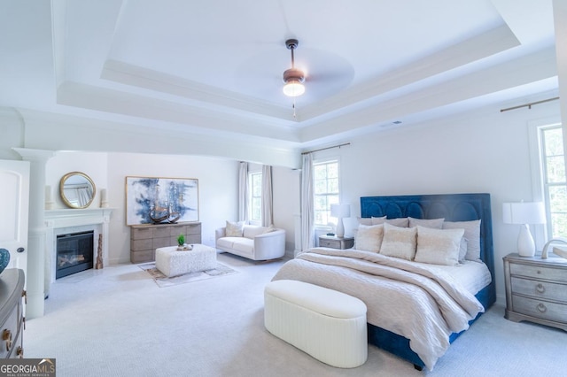 bedroom featuring light carpet, a tray ceiling, multiple windows, and ceiling fan