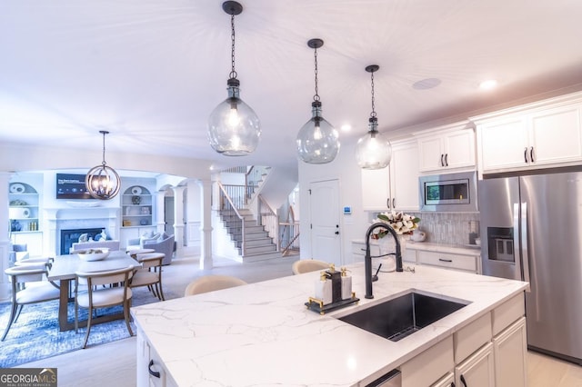 kitchen featuring an island with sink, decorative columns, appliances with stainless steel finishes, and decorative light fixtures