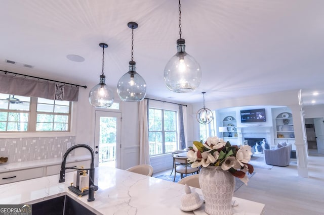 kitchen featuring built in shelves, pendant lighting, light stone countertops, and sink