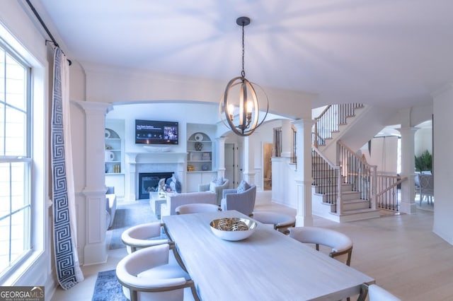 dining room featuring built in shelves, a notable chandelier, light wood-type flooring, and decorative columns