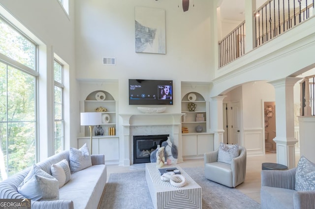 living room with ceiling fan, ornate columns, a high ceiling, and built in shelves