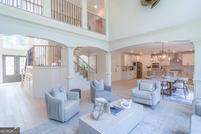 living room featuring light hardwood / wood-style flooring, a high ceiling, decorative columns, and a notable chandelier