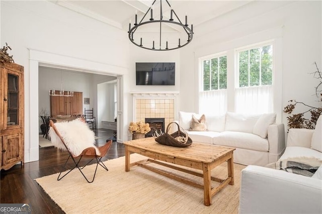 living room with an inviting chandelier, wood-type flooring, beam ceiling, and a tile fireplace