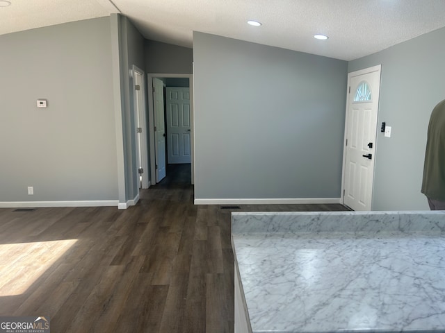 empty room featuring a textured ceiling, vaulted ceiling, and dark wood-type flooring