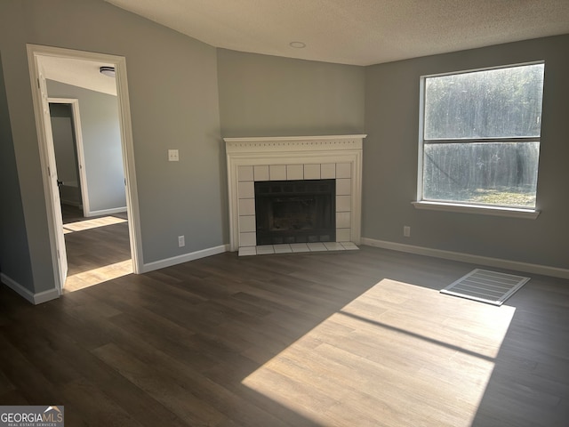 unfurnished living room with a textured ceiling, a tile fireplace, lofted ceiling, and dark wood-type flooring