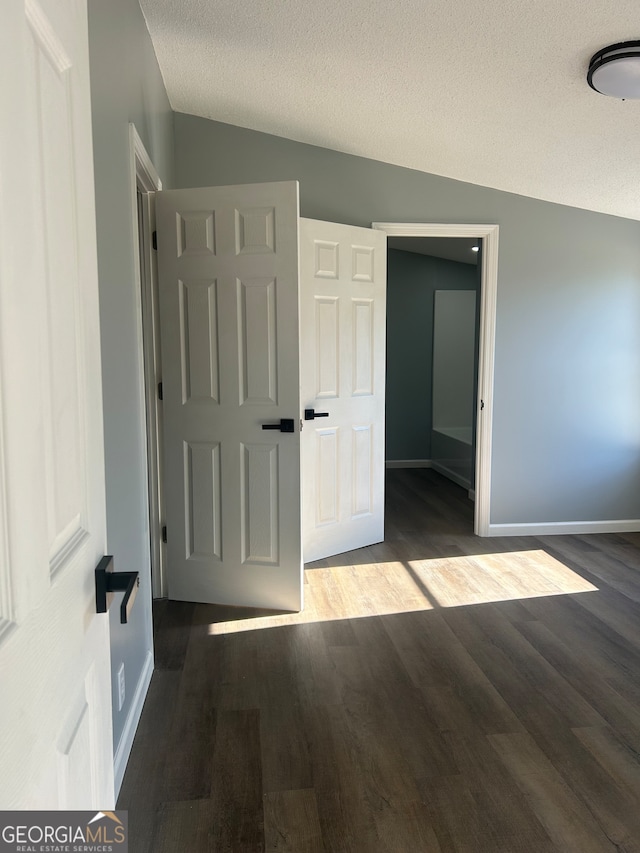 empty room with vaulted ceiling, a textured ceiling, and dark hardwood / wood-style flooring