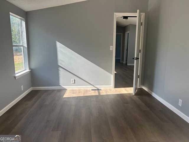 unfurnished room featuring a wealth of natural light, lofted ceiling, a textured ceiling, and dark wood-type flooring