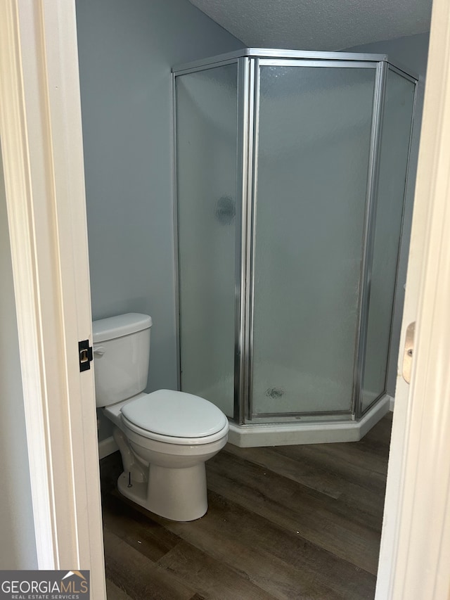 bathroom with wood-type flooring, a textured ceiling, a shower with door, and toilet